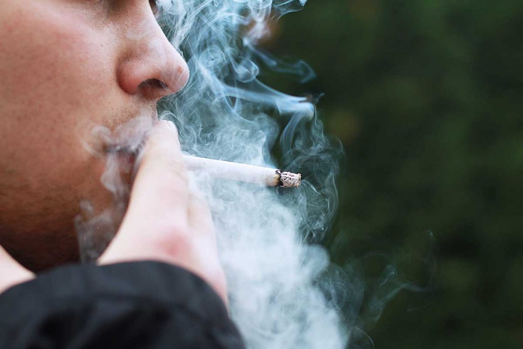 Un homme qui fume une cigarette, ce qui est souvent responsable du cancer du poumon