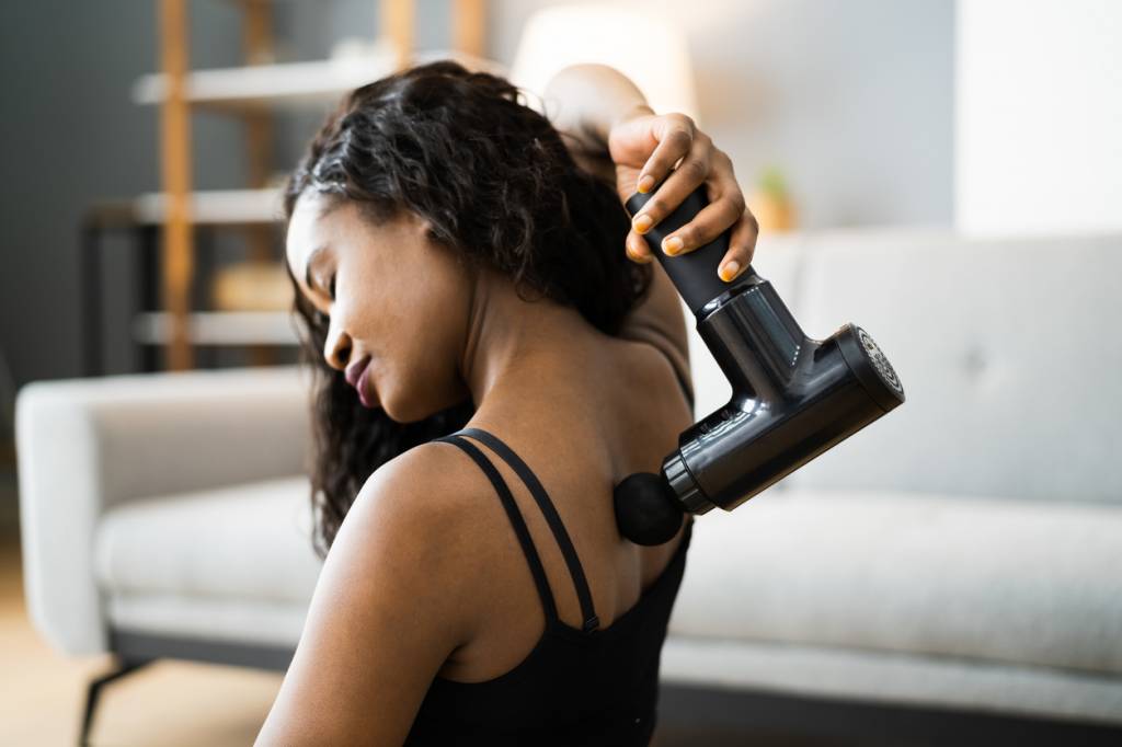 Une femme qui se masse le dos avec un pistolet à massage.