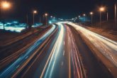 Exposition longue montrant les lumières floues des voitures passant sur une autoroute faiblement éclairée, symbolisant une vision floue causée par l'astigmatisme, dans des tons bleutés profonds et peu saturés.