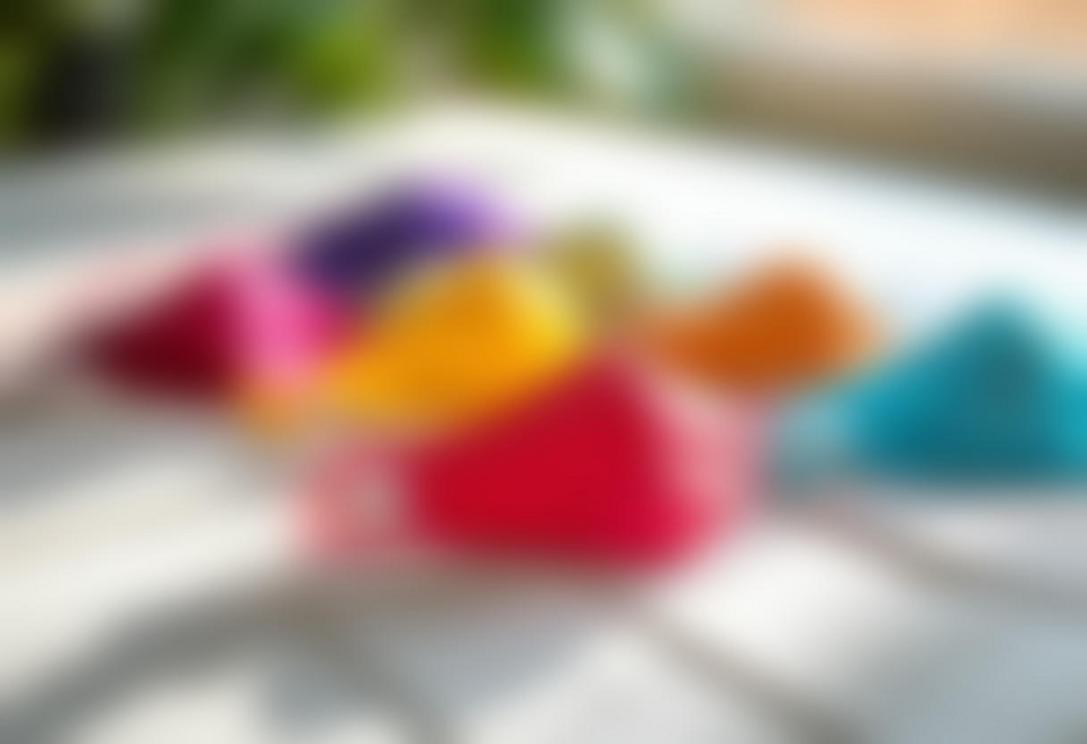Une gamme de masques de visage en tissu tendance et colorés, affichés soigneusement sur une table en bois blanc, illuminés par une lumière naturelle douce.
