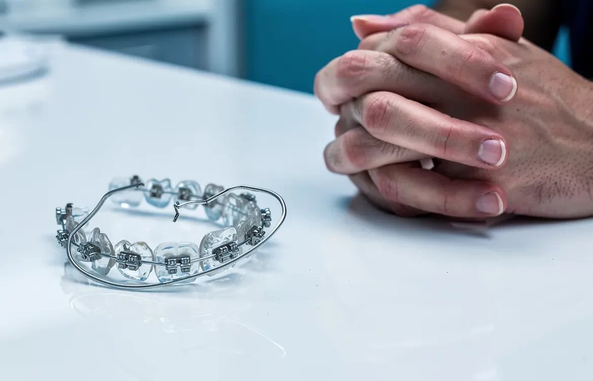 Un appareil dentaire cassé repose près des mains inquiètes d’un patient sur un comptoir de clinique.