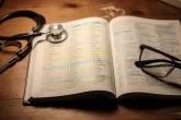 Un dictionnaire médical ouvert présente un tableau des préfixes, suffixes et racines, accompagné d’un stéthoscope et de lunettes sur un bureau en bois.