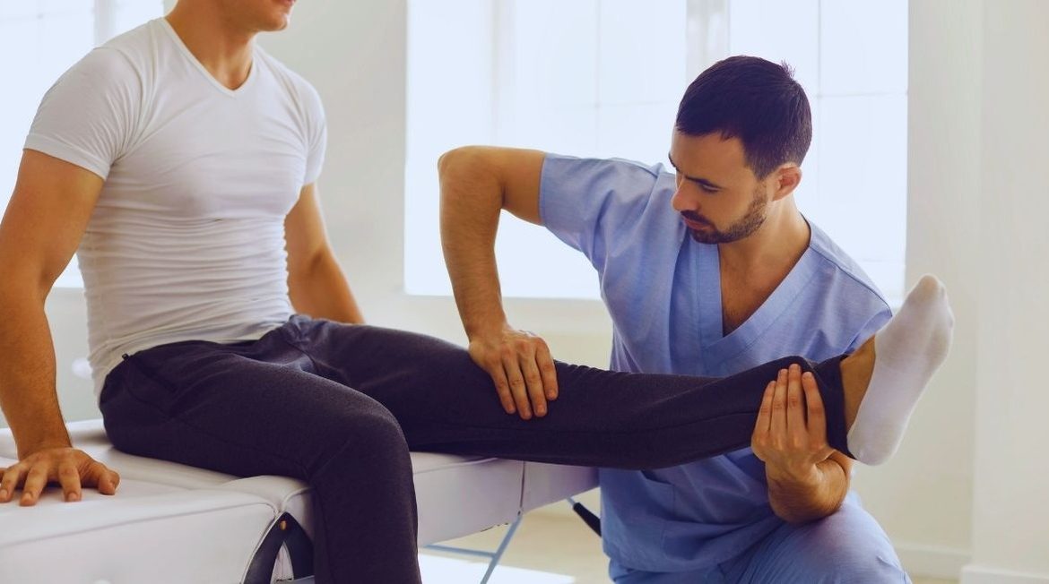 Médecin examinant la mobilité du genou d'un jeune homme assis sur une table d'examen